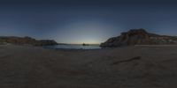 the sun sets on an empty beach with waves crashing toward the rocks, with two small boats out on the water