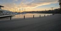 a boat dock and walkway with boats in the water at sunset with the sun going down