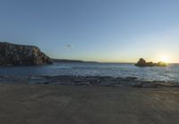 the sun is setting in front of a rocky shoreline and the ocean is below the rocks