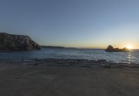 the sun is setting in front of a rocky shoreline and the ocean is below the rocks