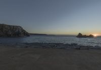 the sun is setting in front of a rocky shoreline and the ocean is below the rocks