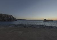 the sun is setting in front of a rocky shoreline and the ocean is below the rocks