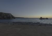 the sun is setting in front of a rocky shoreline and the ocean is below the rocks