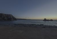 the sun is setting in front of a rocky shoreline and the ocean is below the rocks