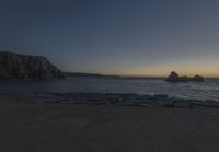 the sun is setting in front of a rocky shoreline and the ocean is below the rocks