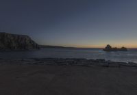 the sun is setting in front of a rocky shoreline and the ocean is below the rocks