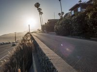 the sun is setting over a coastal street lined with palm trees and stone walling