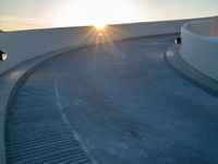 the sun is setting over a curved walkway in the desert style of town parkland