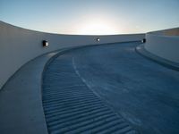 the sun is setting over a curved walkway in the desert style of town parkland