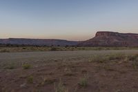 a dirt road passes between some mountains and desert land at sunset with a clear sky