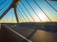 a car driving across a large bridge in the sun setting over the road and the sky