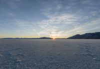 the sun is setting on a frozen lake in a field full of snow, which is vast and filled with fresh white material