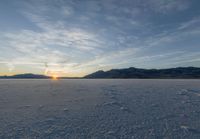 the sun is setting on a frozen lake in a field full of snow, which is vast and filled with fresh white material