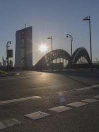 the sun shines brightly on this street near a city bridge and buildings during sunset