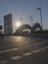 the sun shines brightly on this street near a city bridge and buildings during sunset