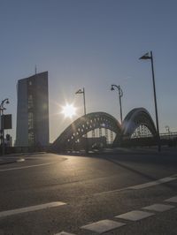 the sun shines brightly on this street near a city bridge and buildings during sunset