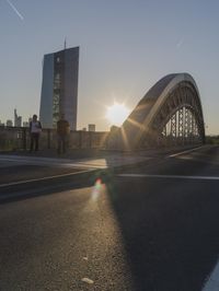 the sun shines brightly on this street near a city bridge and buildings during sunset