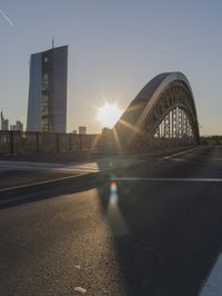 the sun shines brightly on this street near a city bridge and buildings during sunset