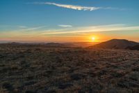 there is a sunset in the horizon on a field with grassy land below the mountains