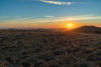 there is a sunset in the horizon on a field with grassy land below the mountains