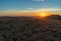 there is a sunset in the horizon on a field with grassy land below the mountains