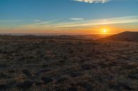 there is a sunset in the horizon on a field with grassy land below the mountains