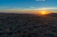 there is a sunset in the horizon on a field with grassy land below the mountains