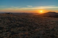 there is a sunset in the horizon on a field with grassy land below the mountains