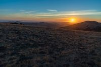 there is a sunset in the horizon on a field with grassy land below the mountains