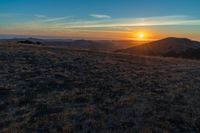 there is a sunset in the horizon on a field with grassy land below the mountains