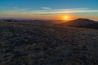 there is a sunset in the horizon on a field with grassy land below the mountains