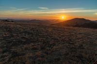 there is a sunset in the horizon on a field with grassy land below the mountains