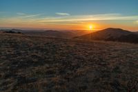 there is a sunset in the horizon on a field with grassy land below the mountains