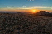 there is a sunset in the horizon on a field with grassy land below the mountains