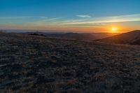 there is a sunset in the horizon on a field with grassy land below the mountains