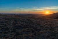 there is a sunset in the horizon on a field with grassy land below the mountains