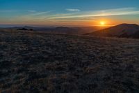 there is a sunset in the horizon on a field with grassy land below the mountains