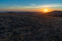 there is a sunset in the horizon on a field with grassy land below the mountains