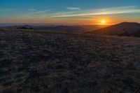 there is a sunset in the horizon on a field with grassy land below the mountains