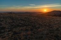 there is a sunset in the horizon on a field with grassy land below the mountains