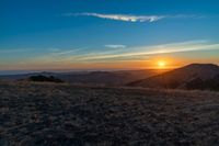 there is a sunset in the horizon on a field with grassy land below the mountains