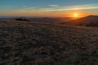 there is a sunset in the horizon on a field with grassy land below the mountains