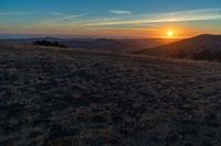 there is a sunset in the horizon on a field with grassy land below the mountains