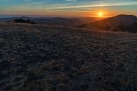 there is a sunset in the horizon on a field with grassy land below the mountains