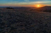 there is a sunset in the horizon on a field with grassy land below the mountains