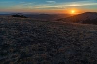 there is a sunset in the horizon on a field with grassy land below the mountains