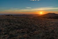 there is a sunset in the horizon on a field with grassy land below the mountains