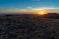 there is a sunset in the horizon on a field with grassy land below the mountains