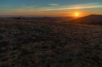 there is a sunset in the horizon on a field with grassy land below the mountains