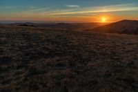 there is a sunset in the horizon on a field with grassy land below the mountains